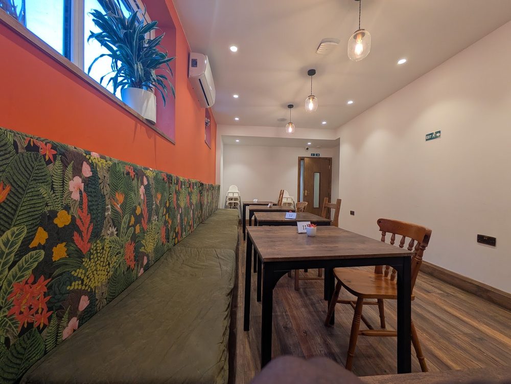 Dining room with terracotta walls, a botanical mural dado, green banquette seating and wooden tables
