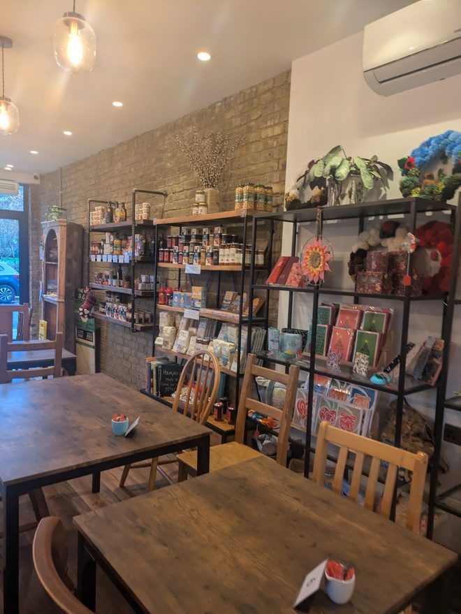 Seating beside a retail shelf of cards, jars and produce against an exposed brick wall